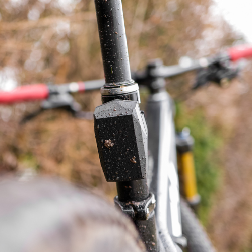 Vista posteriore ravvicinata del reggisella della bicicletta con il tracker GPS Gemstone Bike, manubrio e telaio visibili davanti, con sfondo sfocato della foresta