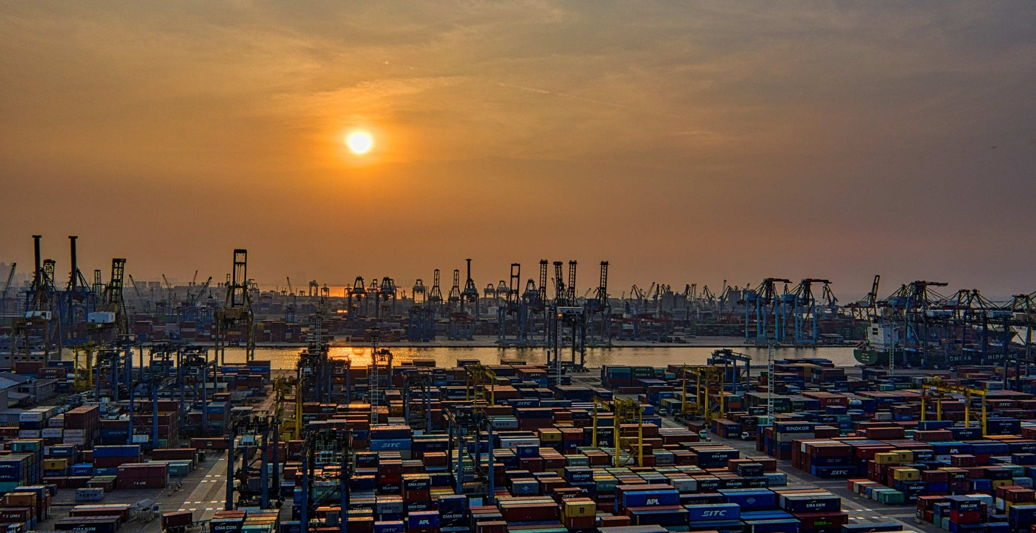 Muted sunset light falling over rows of stacked shipping containers in a vast industrial yard
