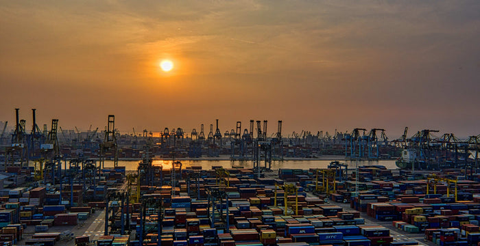 Muted sunset light falling over rows of stacked shipping containers in a vast industrial yard