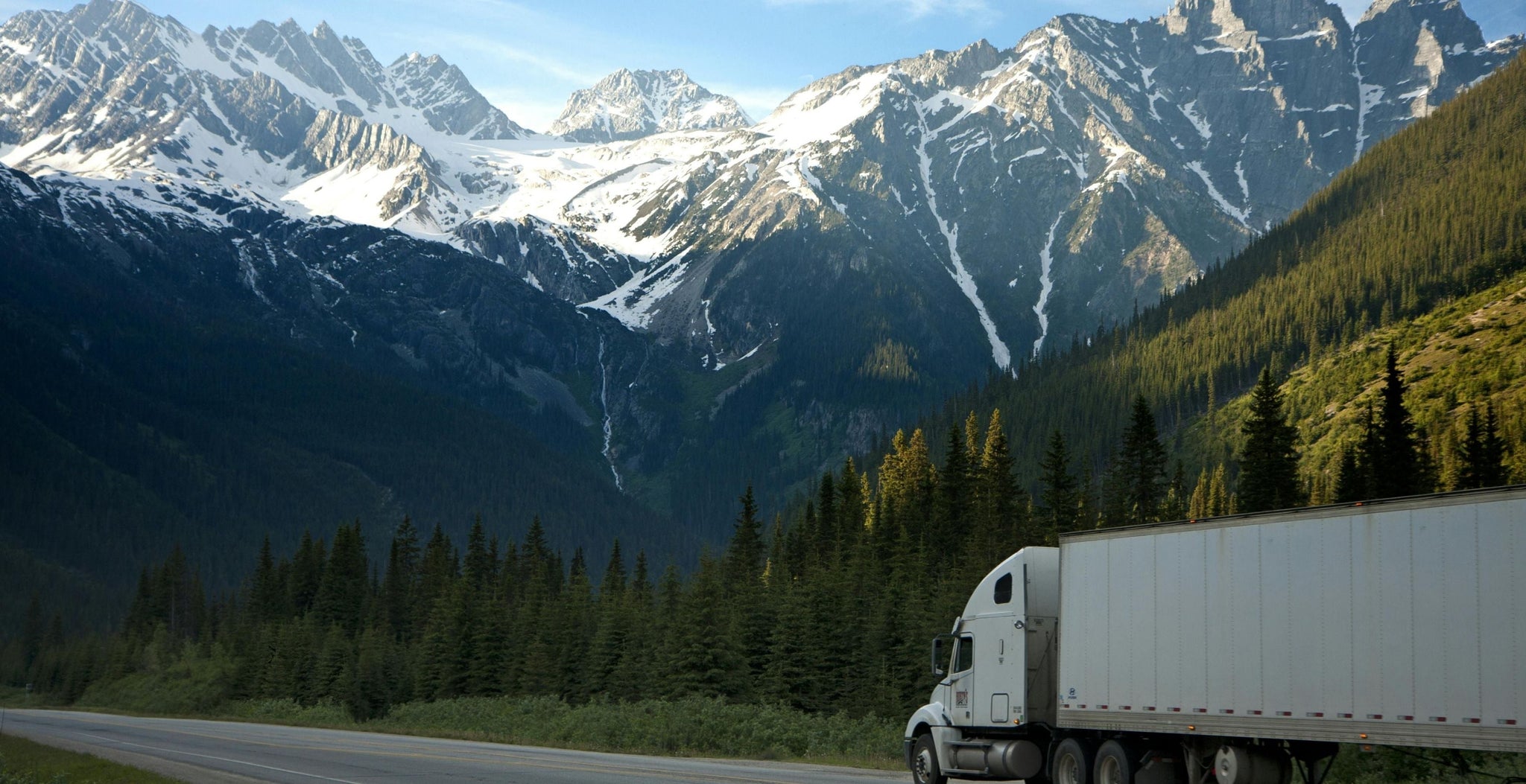 Truck on a road with snow-capped mountains and green trees in the background