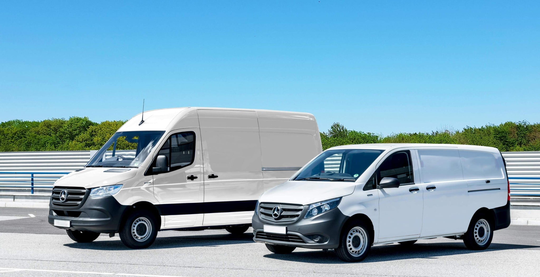 Dwie furgonetki Mercedes-Benz na drodze, w tle czyste, błękitne niebo i zieleń.