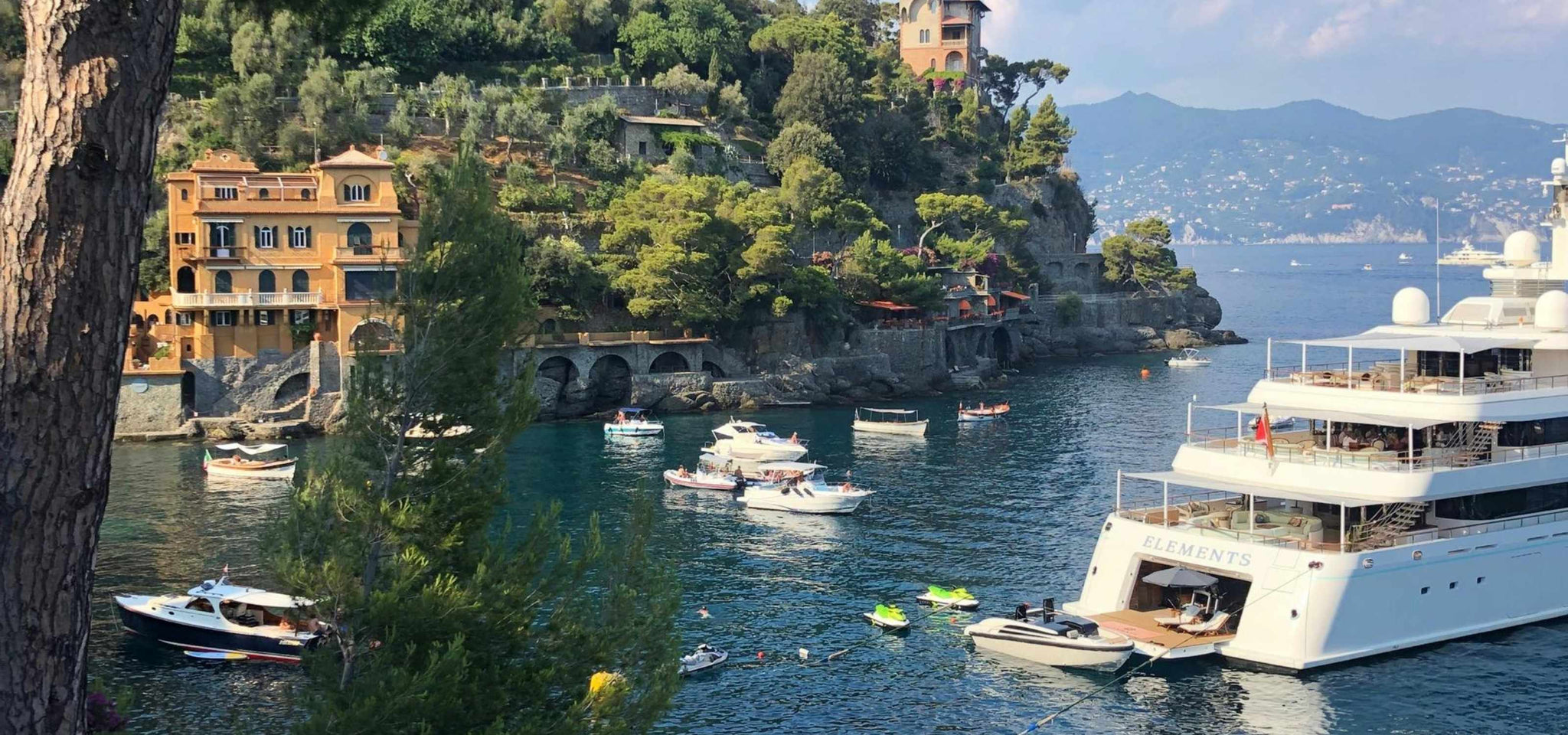 Luksusbåde fortøjet i en malerisk havn med bjerge i baggrunden