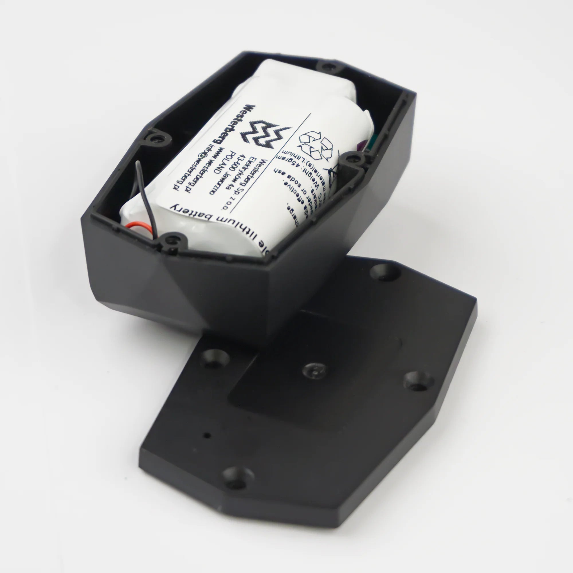 Localizador Gemstone »: carcasa de plástico negro de un dispositivo electrónico con la tapa retirada, en la que se aprecia una batería de iones de litio blanca en su interior, sobre un fondo blanco.