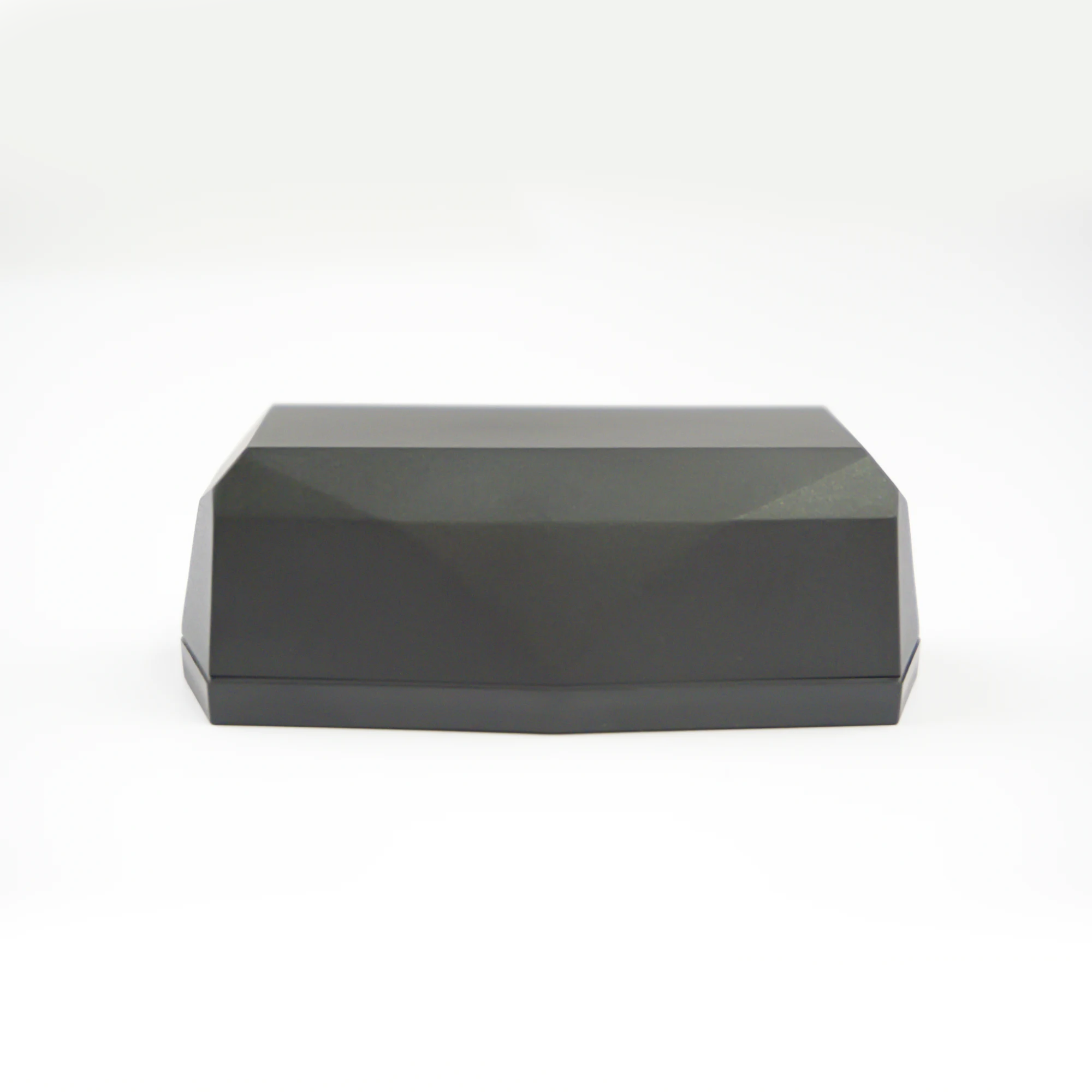 Vista lateral del localizador Gemstone : una caja o recipiente geométrico negro con facetas, sobre un fondo blanco y limpio de estudio.
