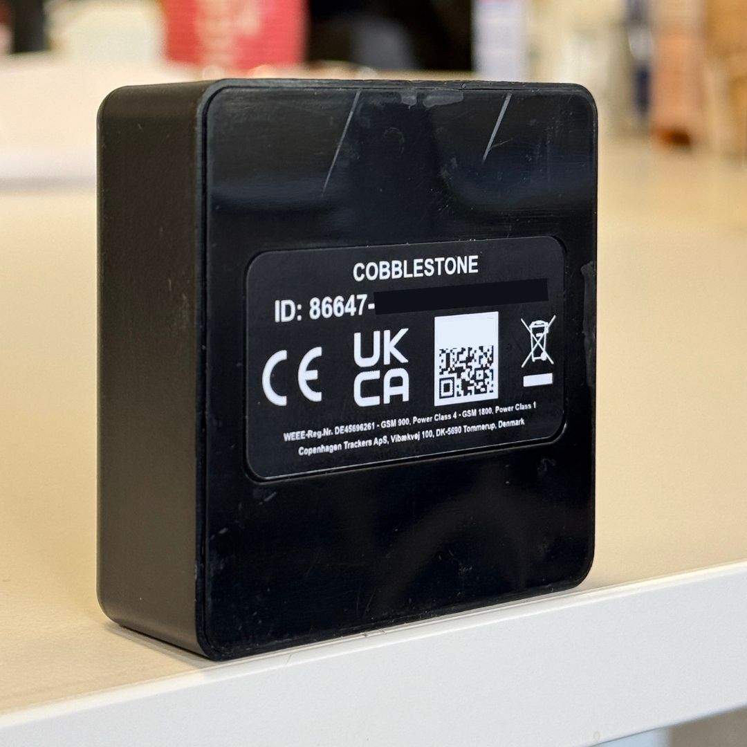 Den svarta sidan av Cobblestone Outlet GPS Tracker mot en suddig bakgrund