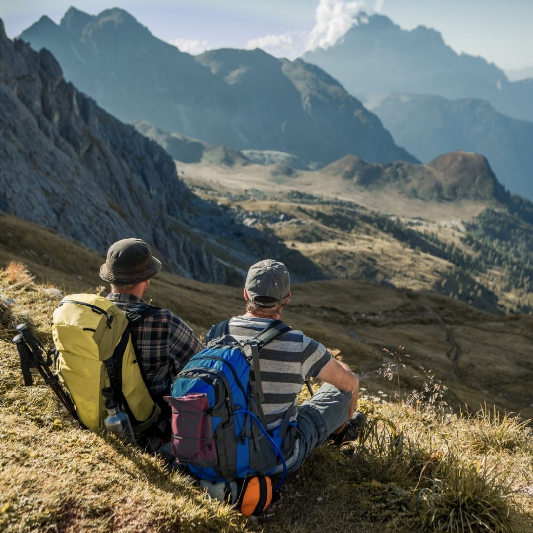 Two hikers with backpacks sitting on a mountain overlooking a valley.