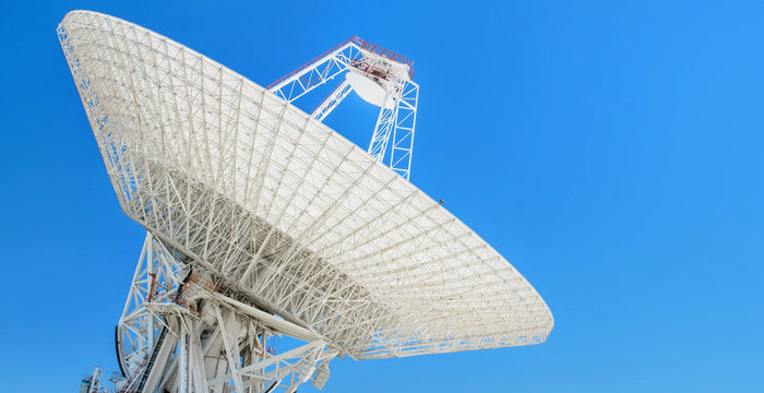 Große Satellitenschüssel, die in den Himmel zeigt, mit einem klaren blauen Himmel im Hintergrund.