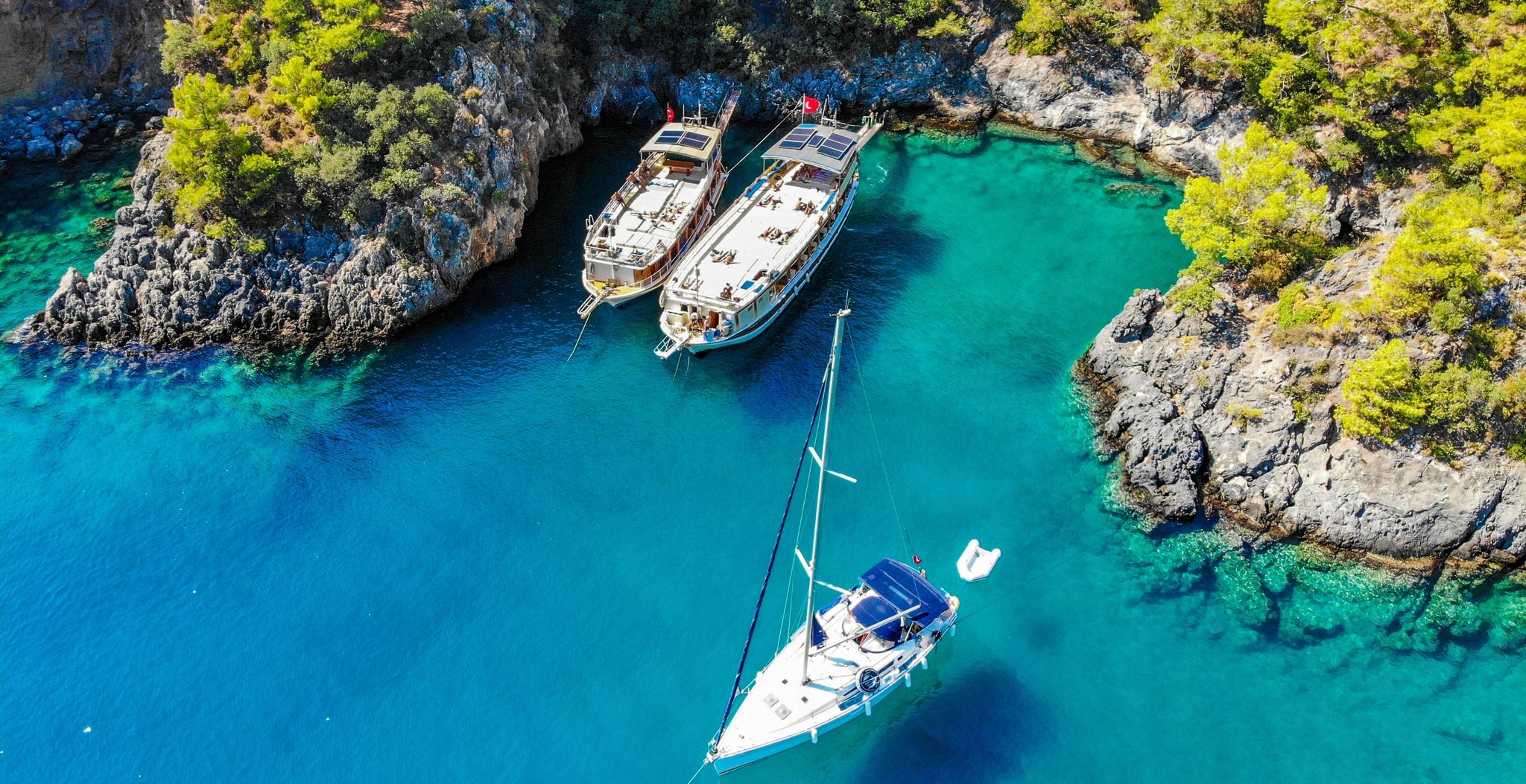 Drei große Segelboote in einer geschützten Bucht mit klarem blaugrünem Wasser und hellgrünen Bäumen am Ufer
