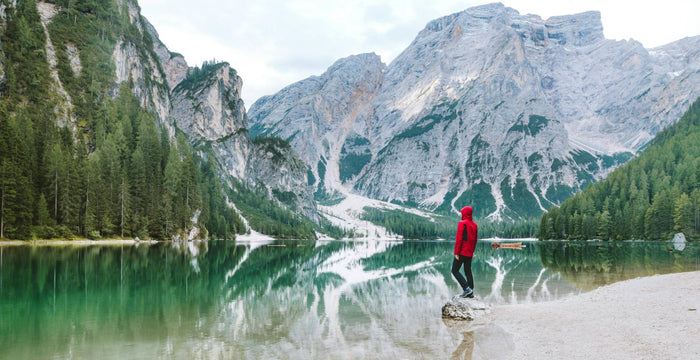 Personne debout dans un paysage norvégien avec une rivière, une forêt et des montagnes en arrière-plan.