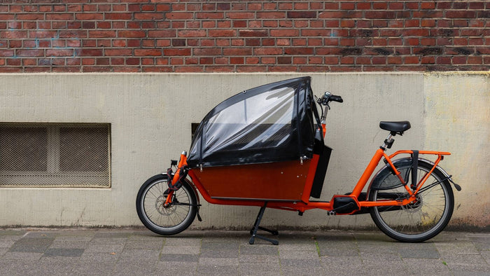 Vélo cargo orange placé contre un mur de briques, le gps traceur Gemstone Bike est placé sur la tige de selle.