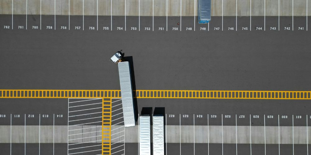 Bovenaanzicht van een grote parkeerplaats met enkele vrachtwagens.