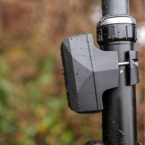 Nærbilde av en sykkelsetepinne med Gemstone Sykkel-GPS-tracker dekket av vanndråper, med en skogkledd bakgrunn